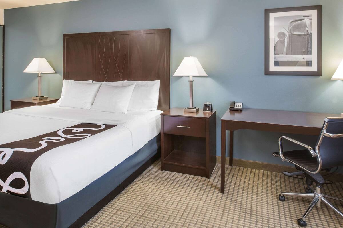 A hotel room with a large bed, two bedside tables with lamps, a desk, and a chair.