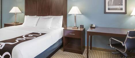 Una habitación de hotel con cama, mesitas de noche con lámparas, escritorio y una silla.
