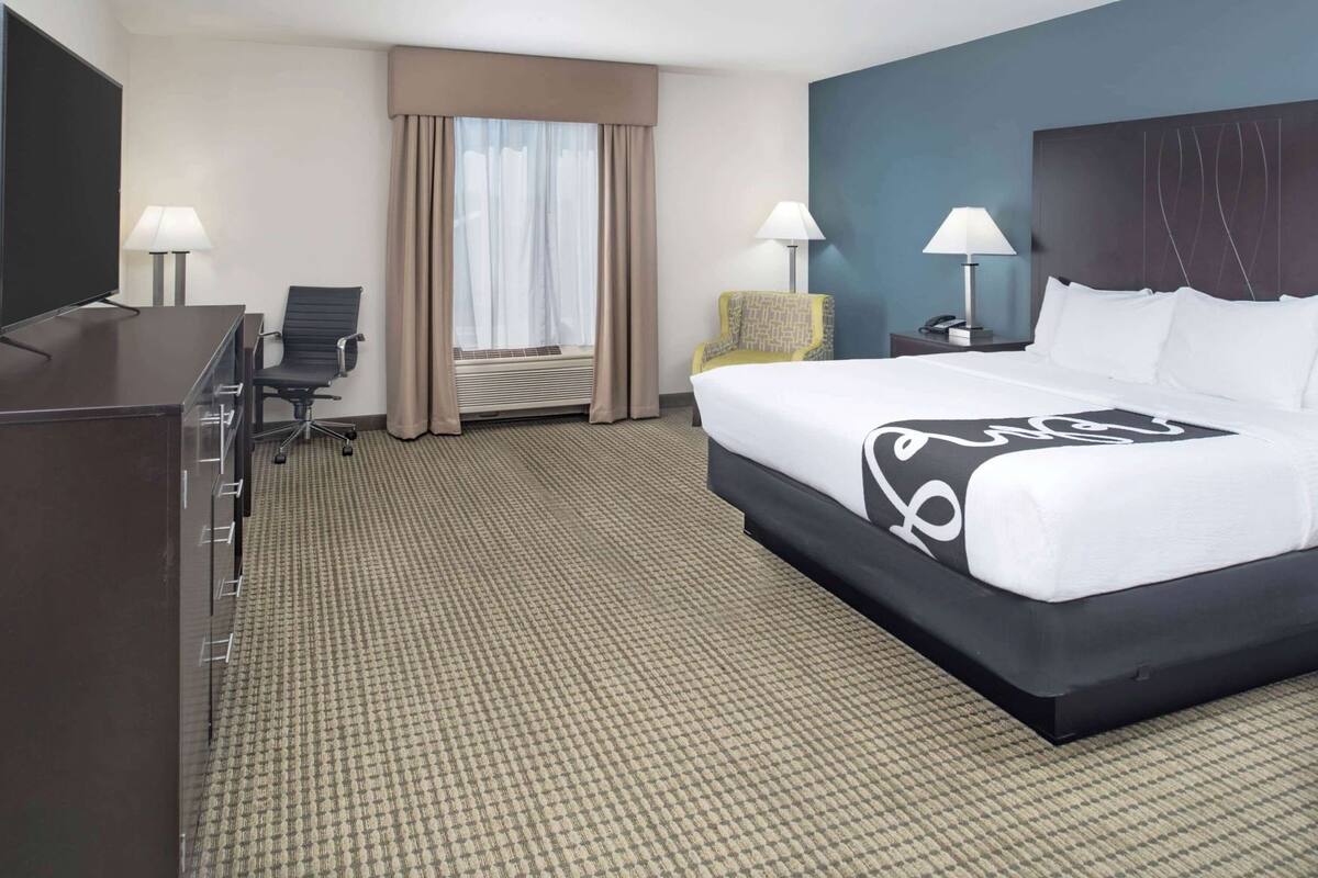 A hotel room with a bed, desk, chair, lamps, and a television.