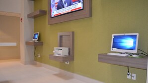 Una stanza con una televisione fissata al muro che mostra un notiziario, un computer su uno scaffale e una stampante su un altro.