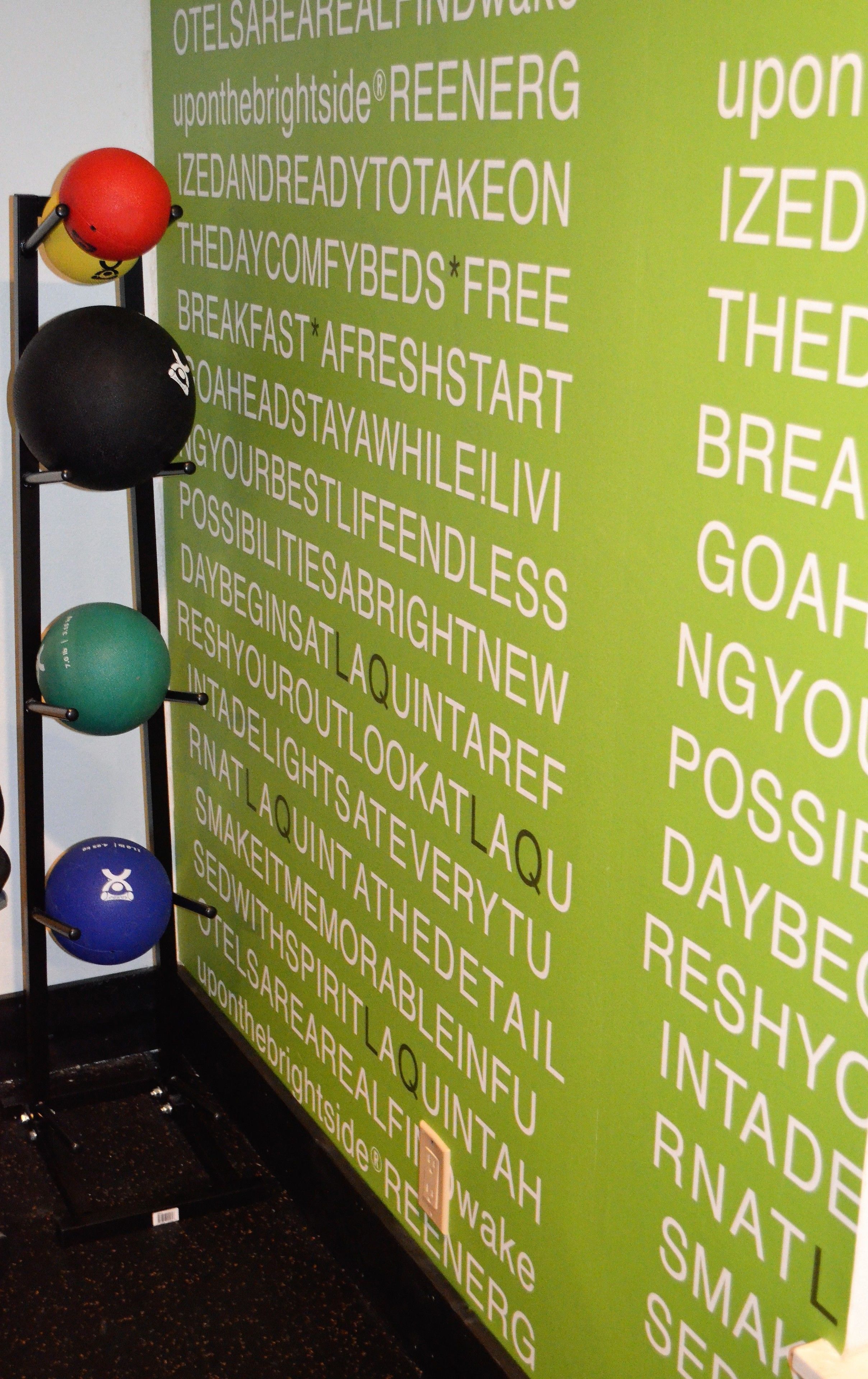 Un mur sur lequel est affichée une liste de phrases motivantes et un présentoir rempli de ballons d’exercice.