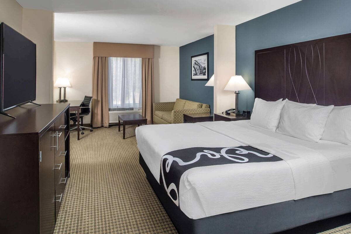 A hotel room with a large bed, a desk with a chair, a television, and a window with curtains.