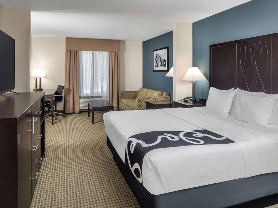 A hotel room with a bed, a desk, a chair, a TV, and a window with curtains.