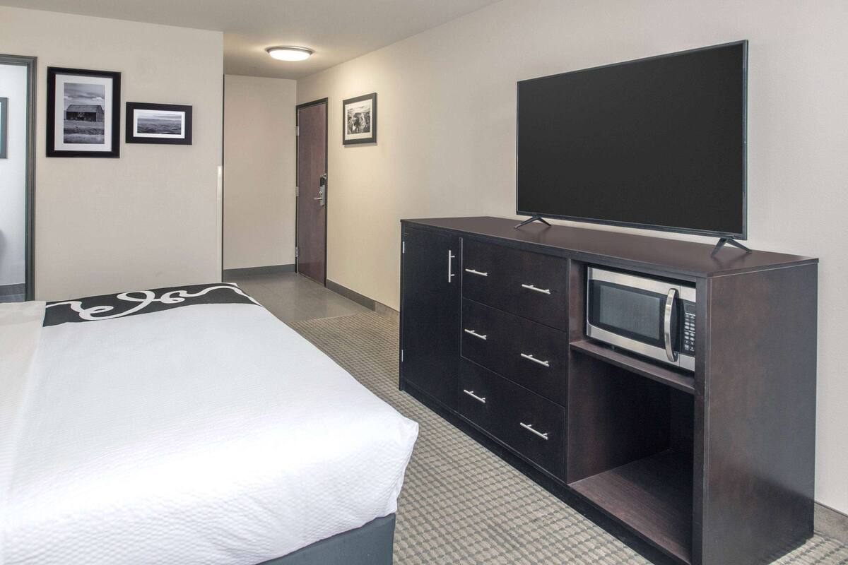 A hotel room with a bed, a dark wooden cabinet with a microwave, and framed pictures on the wall.