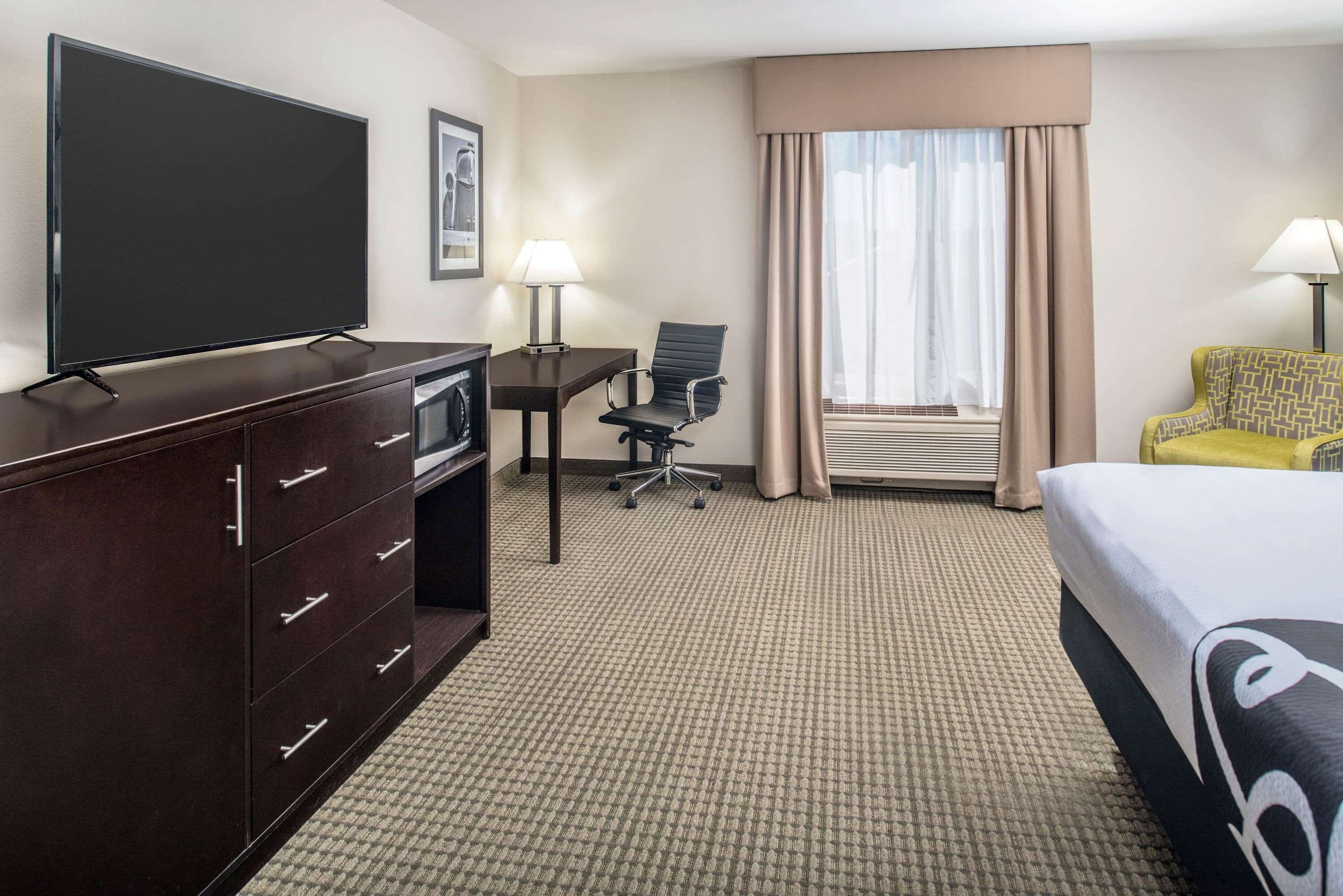 A hotel room with a flat-screen TV, a desk with a chair, a bed, and two lamps.