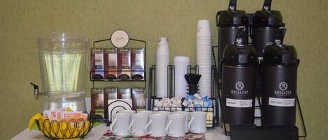 Una estación de café con cafetera, tazas y un cesto de cápsulas de café.