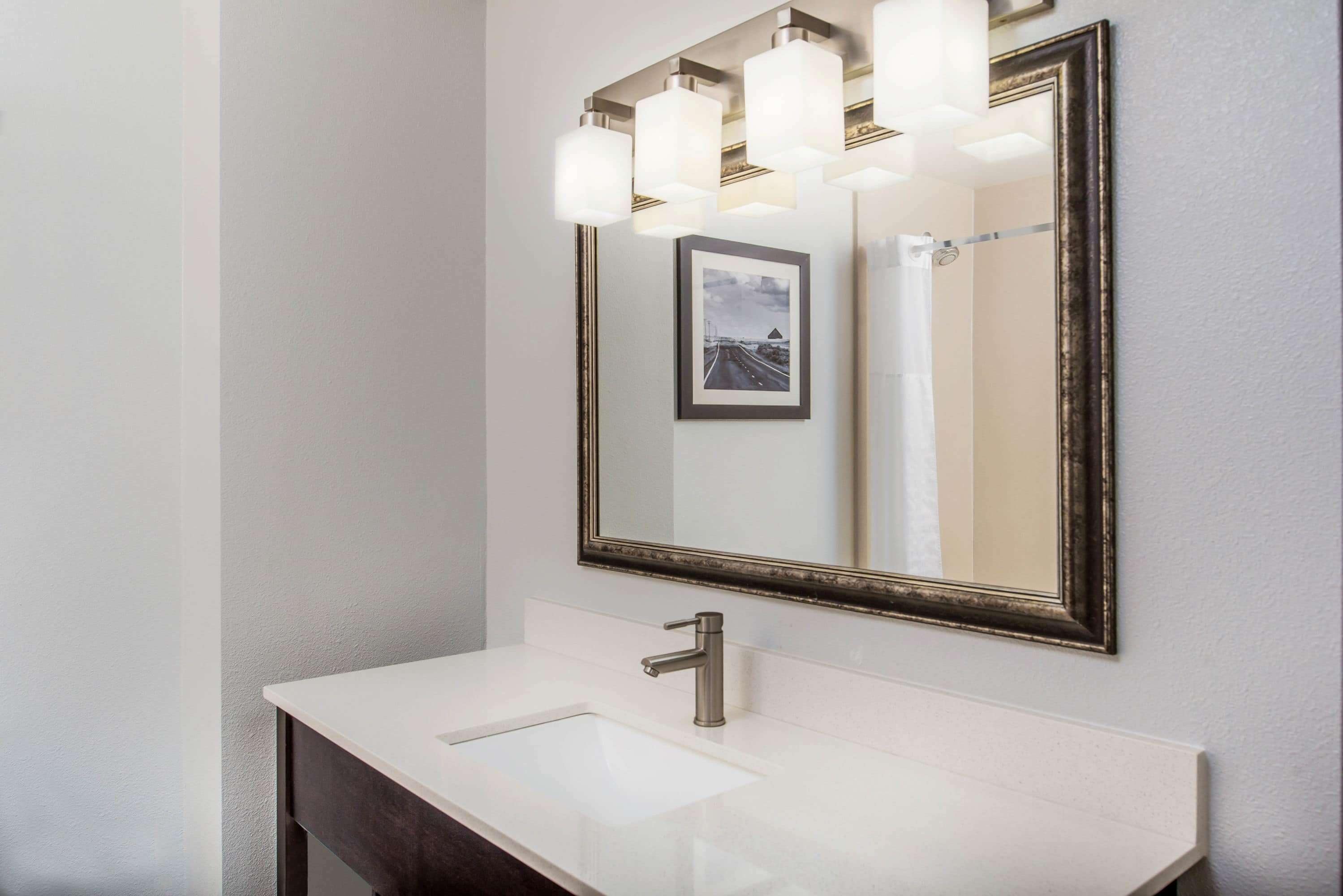 A bathroom with a white sink, a large mirror with a black frame, and a picture on the wall.