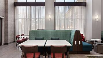 Uma sala de jantar moderna com uma mesa comprida, cadeiras estofadas vermelhas e um sofá verde estampado.
