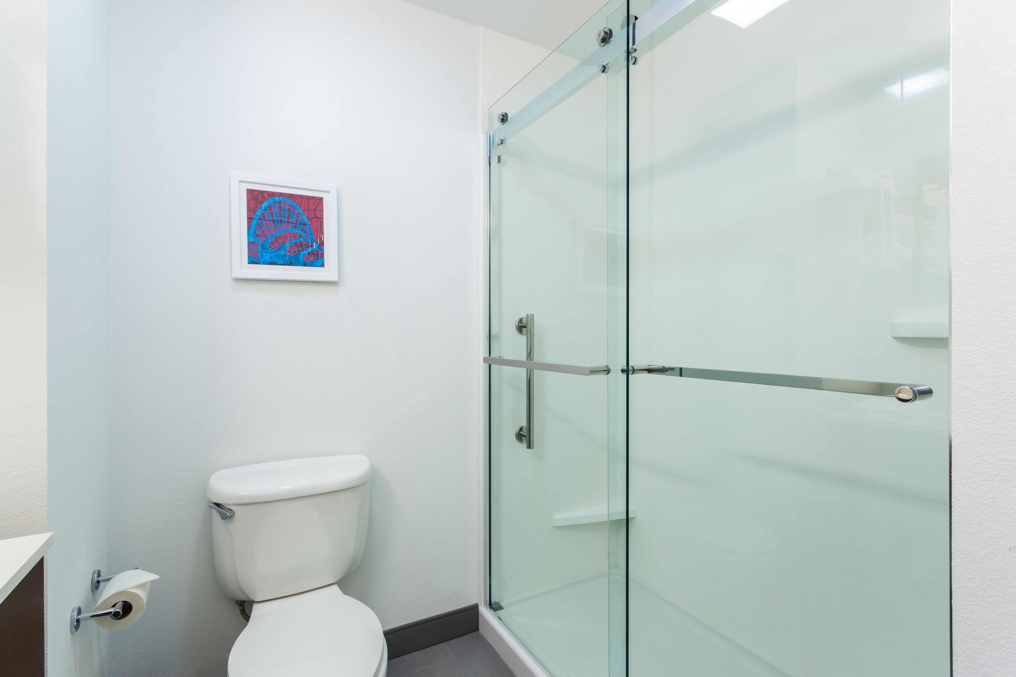 A bathroom with a glass shower enclosure, a white toilet, and a framed artwork on the wall.