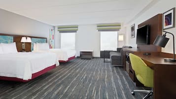 A hotel room with two beds, a desk with a chair, a TV, and a window with blinds.