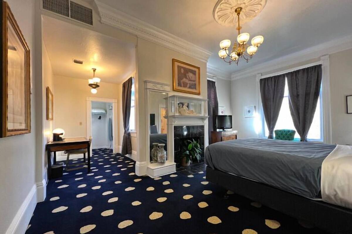 A hotel room with a large bed, a fireplace, a mirror, and a chandelier.