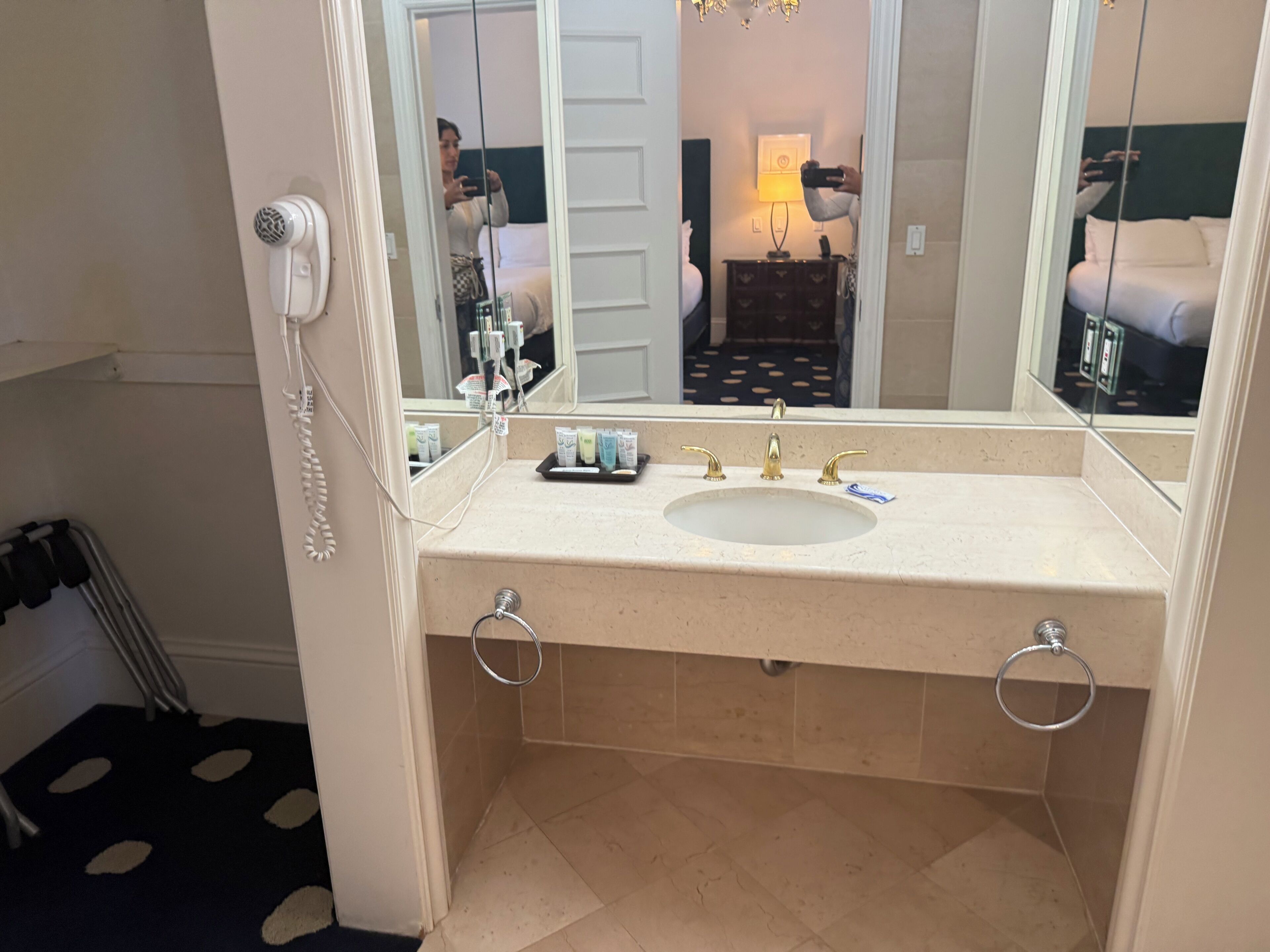 A hotel bathroom with a sink, mirror, and a hairdryer on the wall.