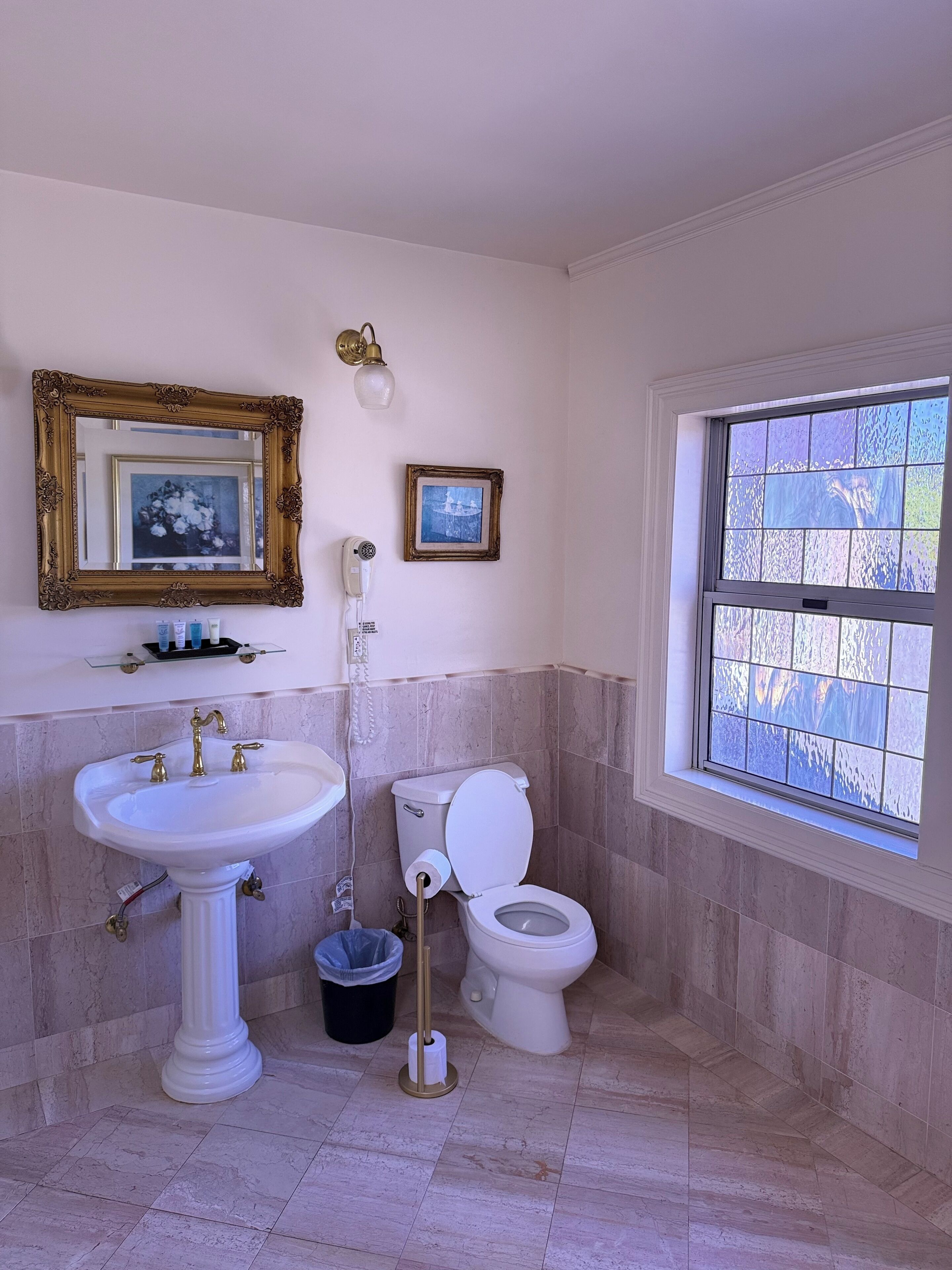 Baño con lavamanos pedestal, inodoro y ventana con vistas.