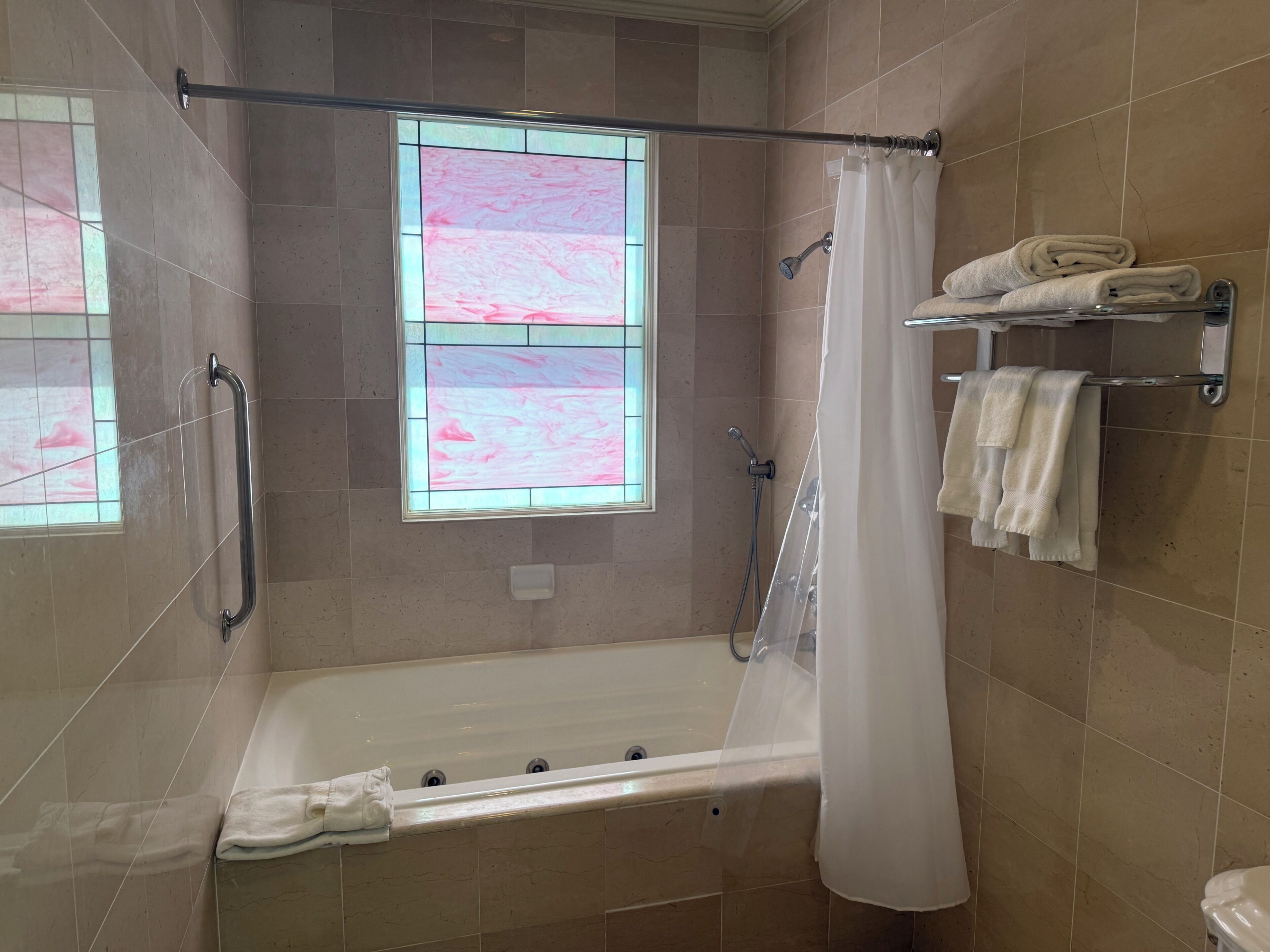 Une salle de bain avec une baignoire, une douche, un rideau de douche en verre et une fenêtre ornée d’un motif rose.