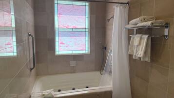 Une salle de bain avec une baignoire, une douche, un rideau de douche en verre et une fenêtre ornée d’un motif rose.