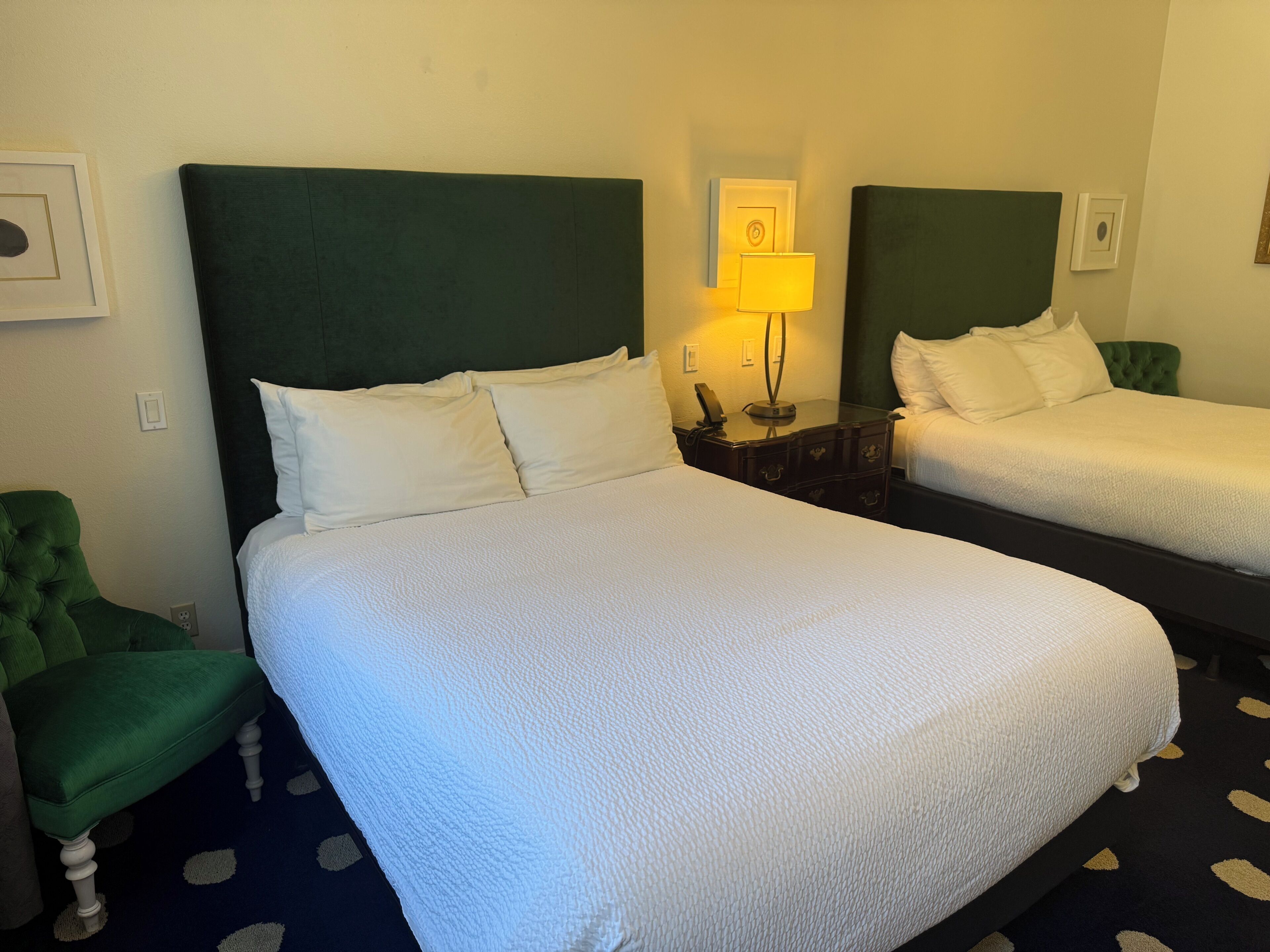 Et hotelværelse med to senge, en grøn lænestol, et natbord med lampe og et billed på væggen.