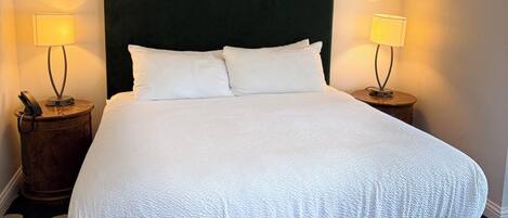 Una cama bien hecha con un cabecero oscuro, dos lámparas de noche y una alfombra de lunares.