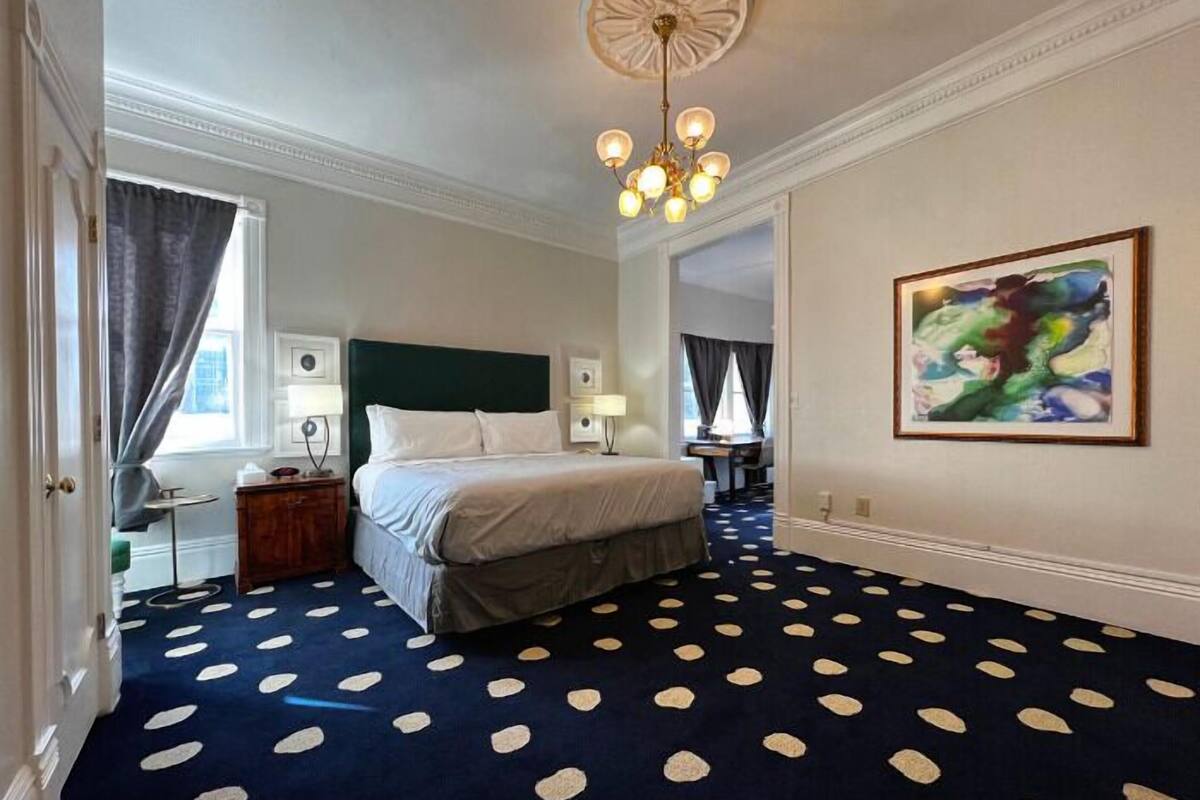 A hotel room with a large bed, a chandelier, a painting on the wall, and a polka dot carpet.