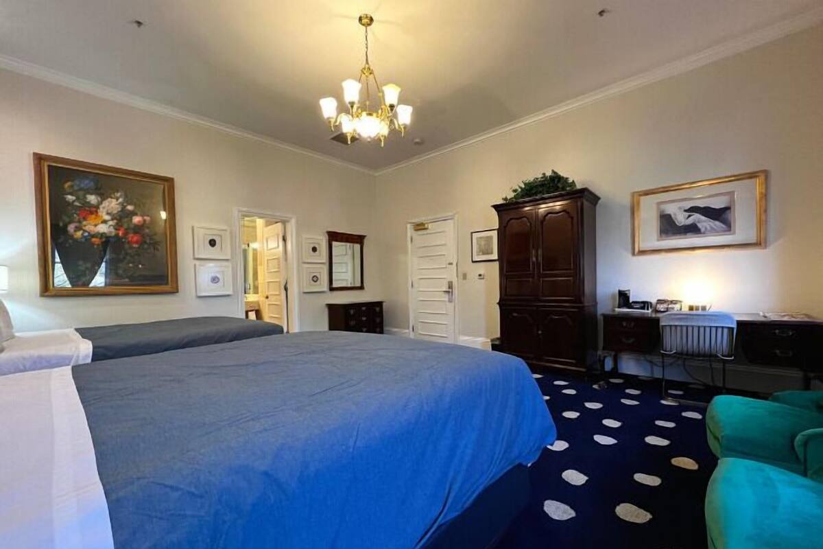 A bedroom with a large bed, a desk with a chair, a cabinet, and a chandelier.
