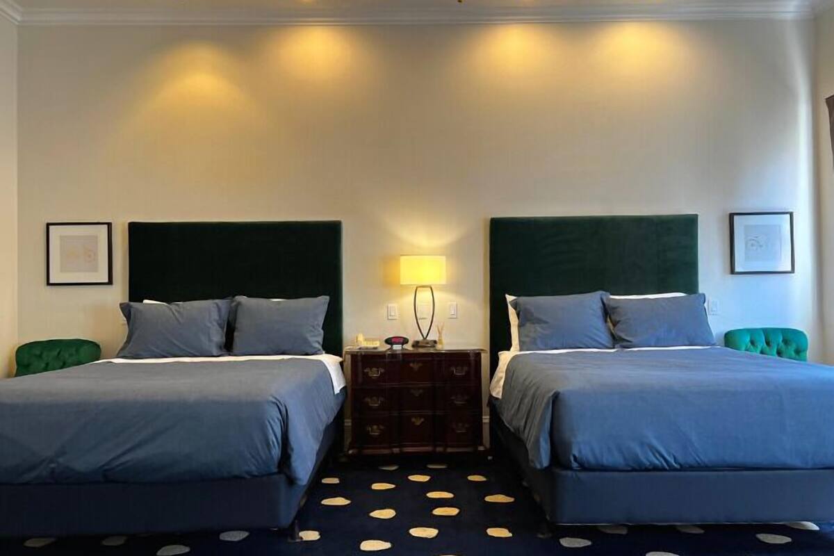 A hotel room with two beds, a nightstand, a lamp, and a polka dot carpet.