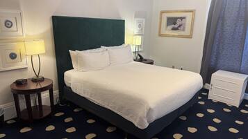 A hotel room with a bed, bedside lamps, a nightstand, a small cabinet, and a patterned carpet.