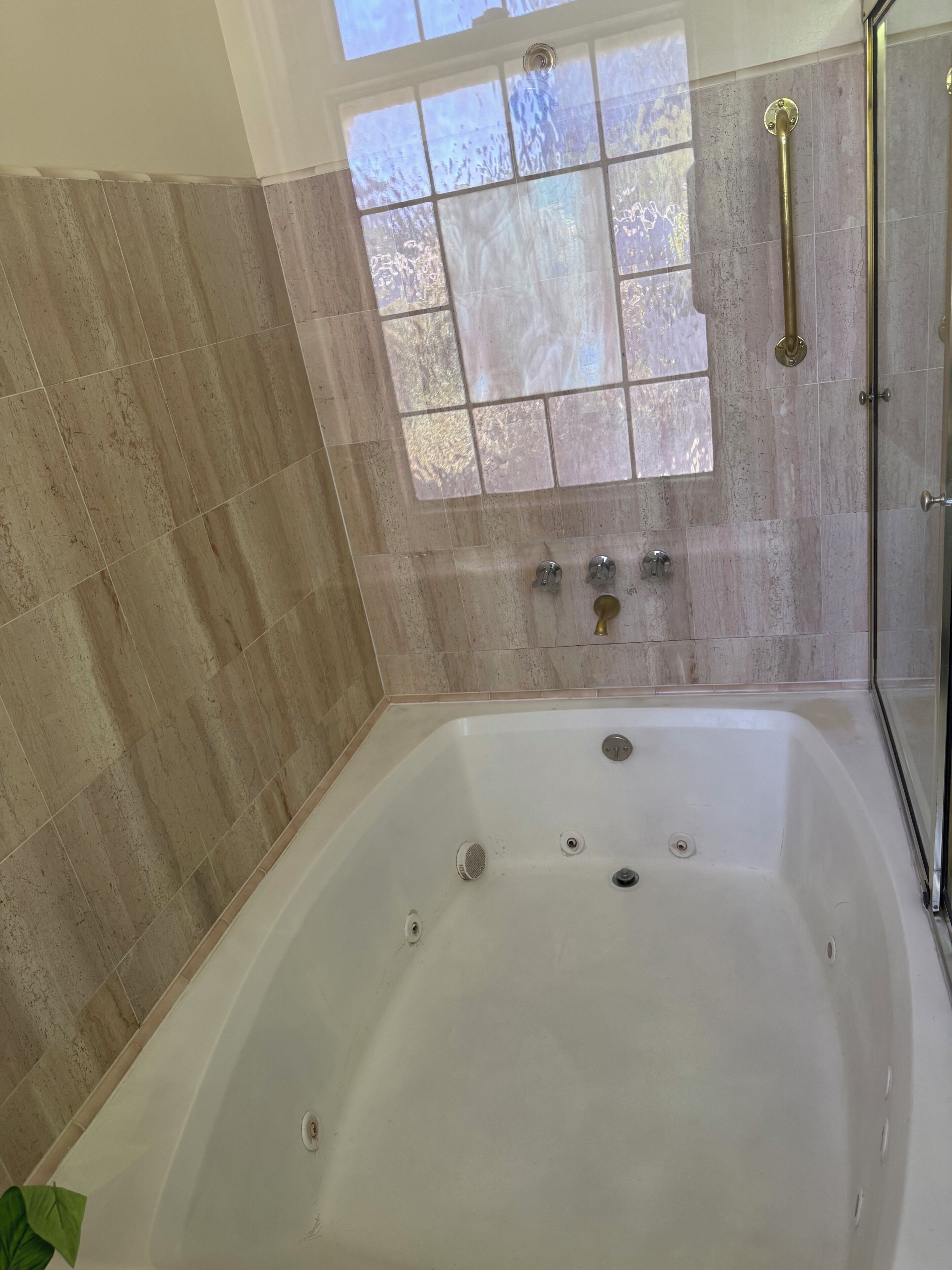 Baño con una bañera grande, cabina de ducha de vidrio y ventana con paneles esmerilados.