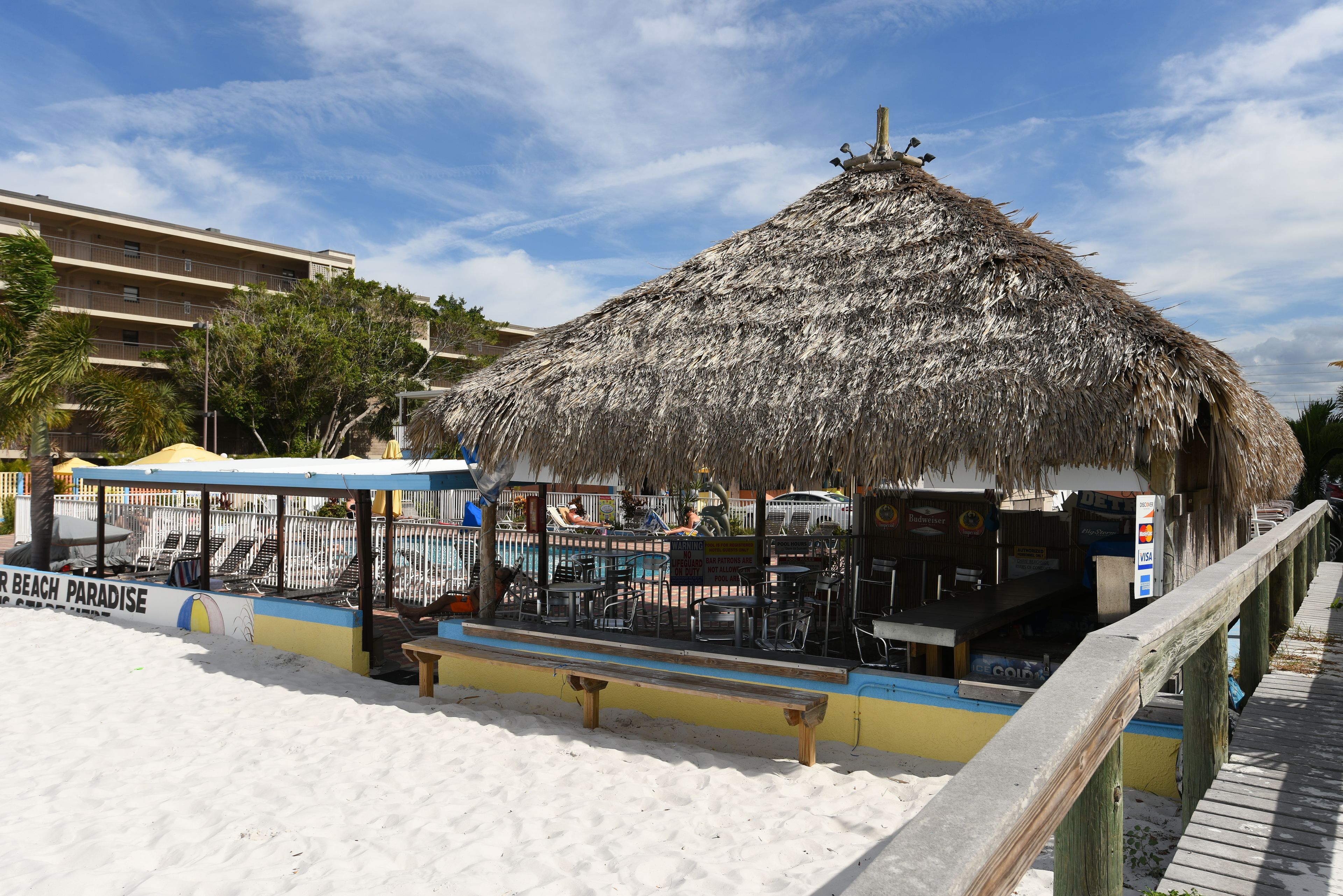 A beachside restaurant with a thatched roof, outdoor seating, and a pool area.