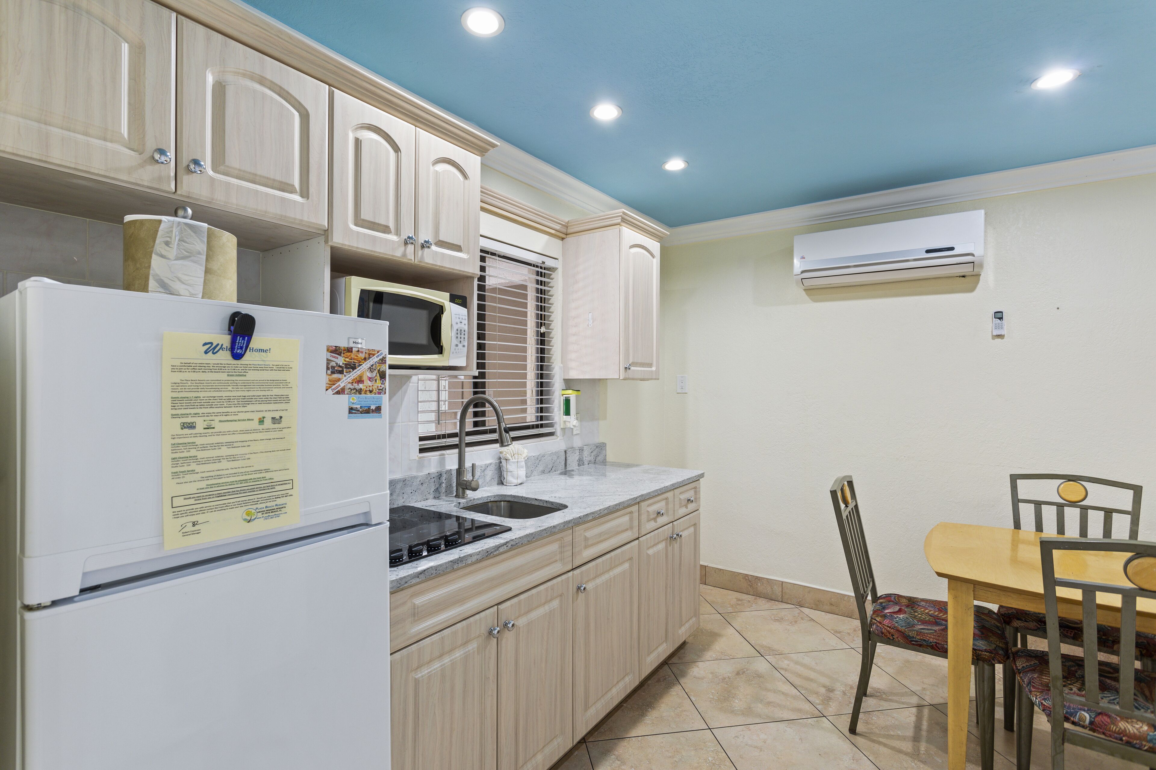 Una cocina con armarios de madera, un refrigerador blanco, un microondas y una mesa de comedor con sillas.