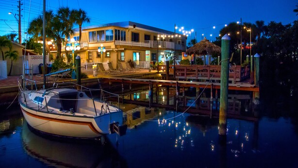 A waterfront property with a docked boat, a balcony with lights, and a thatched-roof structure.