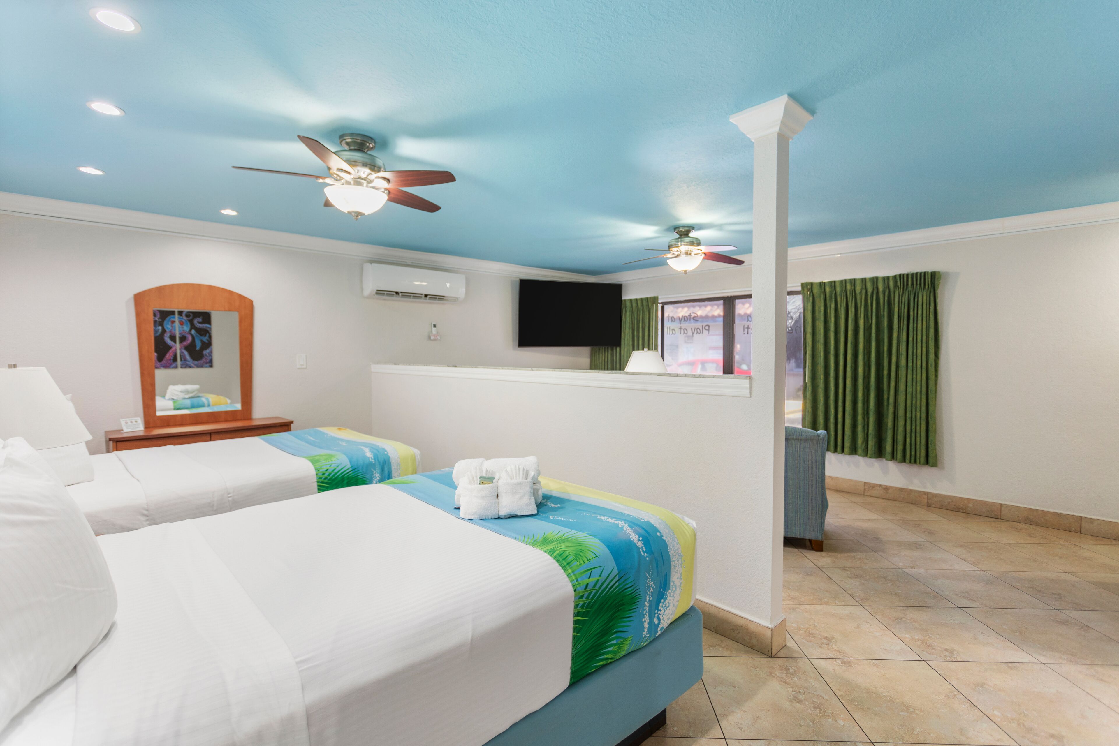 A hotel room with two beds, a ceiling fan, a flat-screen TV, and a window with curtains.