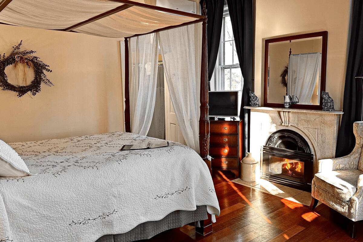 A bedroom with a four-poster bed, a fireplace, and a chair.