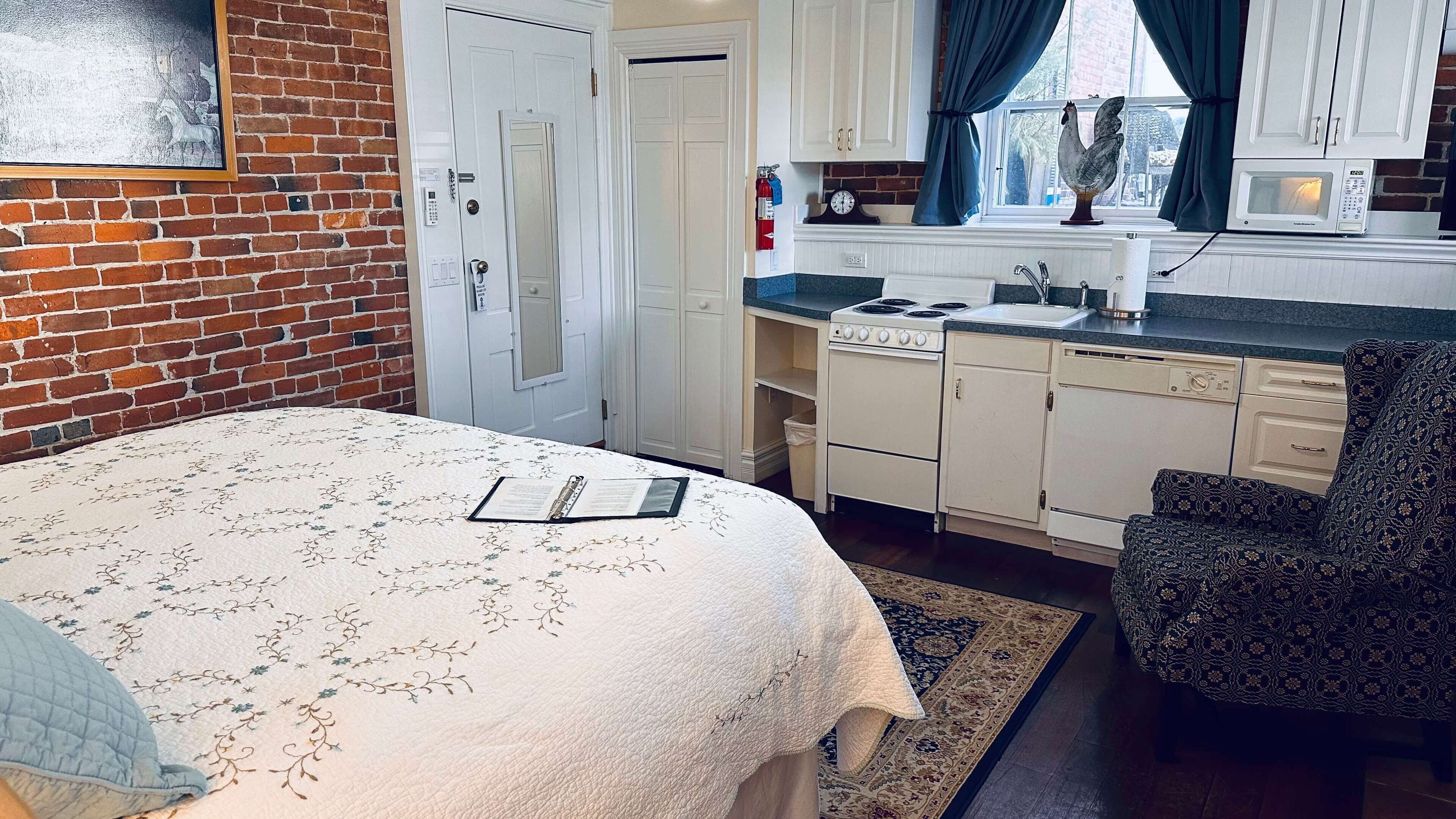 A bedroom with a bed, a bedside table, a nightstand, a window with curtains, and a view of a brick wall.