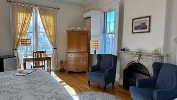 A room with a bed, two armchairs, a wooden cabinet, a fireplace, and a table with a lamp.