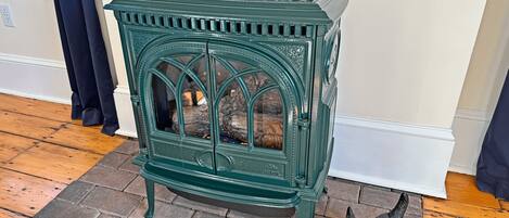 A green cast iron stove with a glass door, placed on a wooden floor with a brick border.