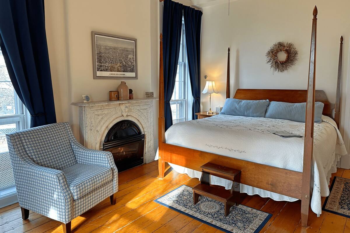 A bedroom with a four-poster bed, a fireplace, a chair, and a rug.