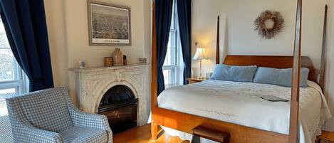 A bedroom with a four-poster bed, a fireplace, a chair, and a rug.