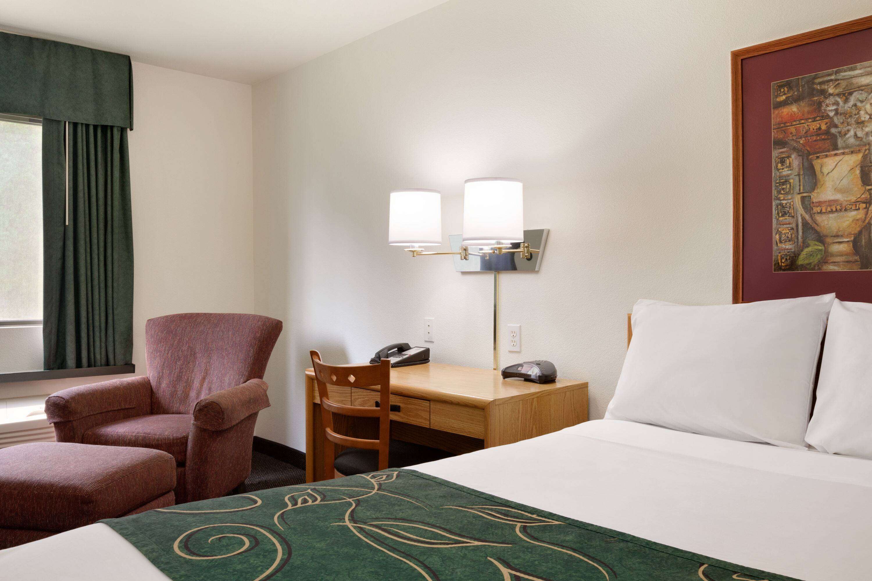 A hotel room with a bed, a desk, a chair, a telephone, and a wall-mounted lamp.