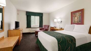 A hotel room with a bed, a desk, a chair, a TV, a lamp, and a window with curtains.
