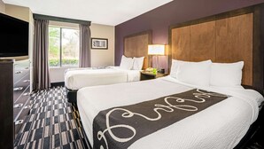A hotel room with two beds, a TV, a desk with a lamp, and a window with curtains.