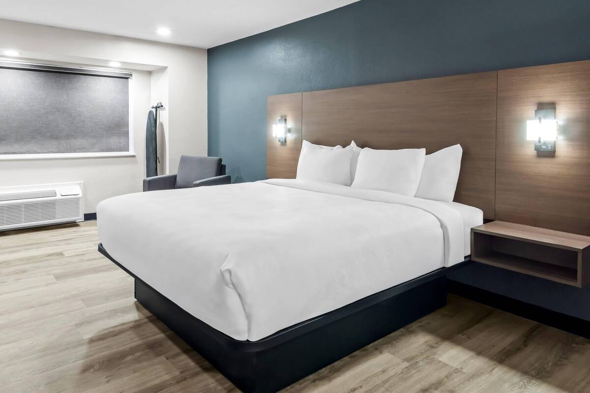 Una camera d'albergo moderna con un letto grande, comodini integrati e un lampadario fissato alla parete.
