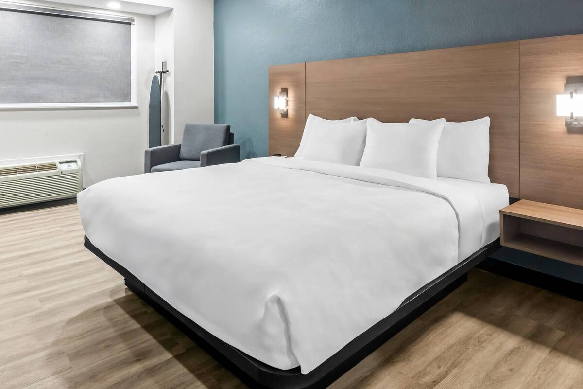 Una camera d'albergo moderna con un letto grande, un comodino, una sedia e un portalampada a parete.