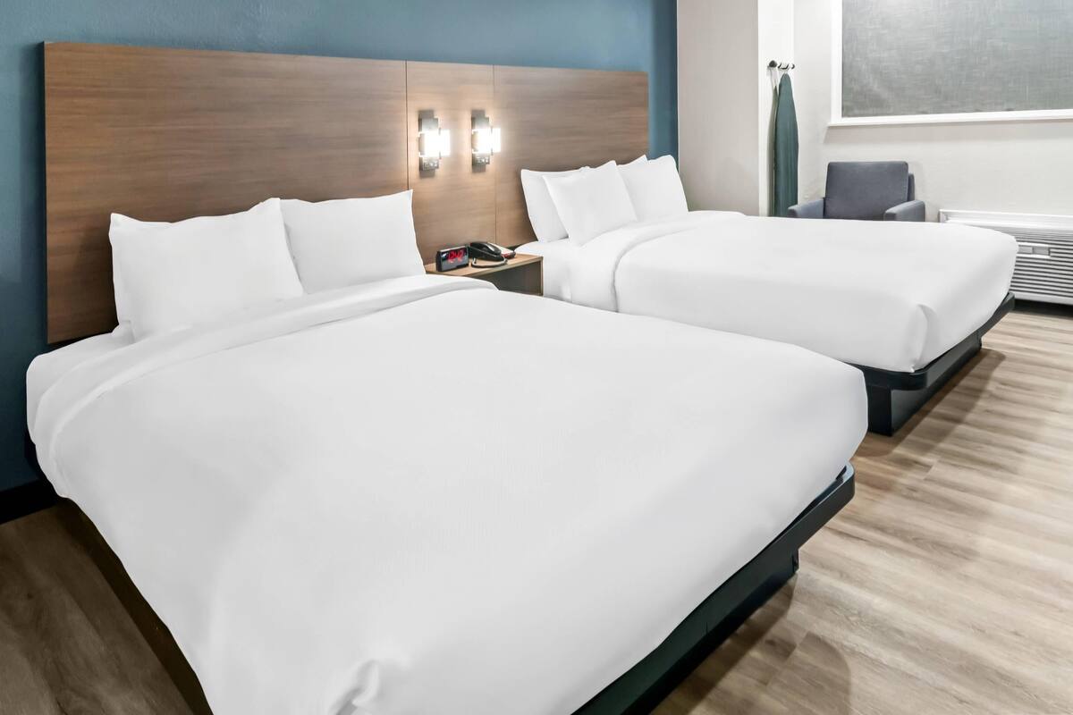 Una camera d'albergo con due letti, una testiera in legno, lampade da comodino, un comodino e una finestra.