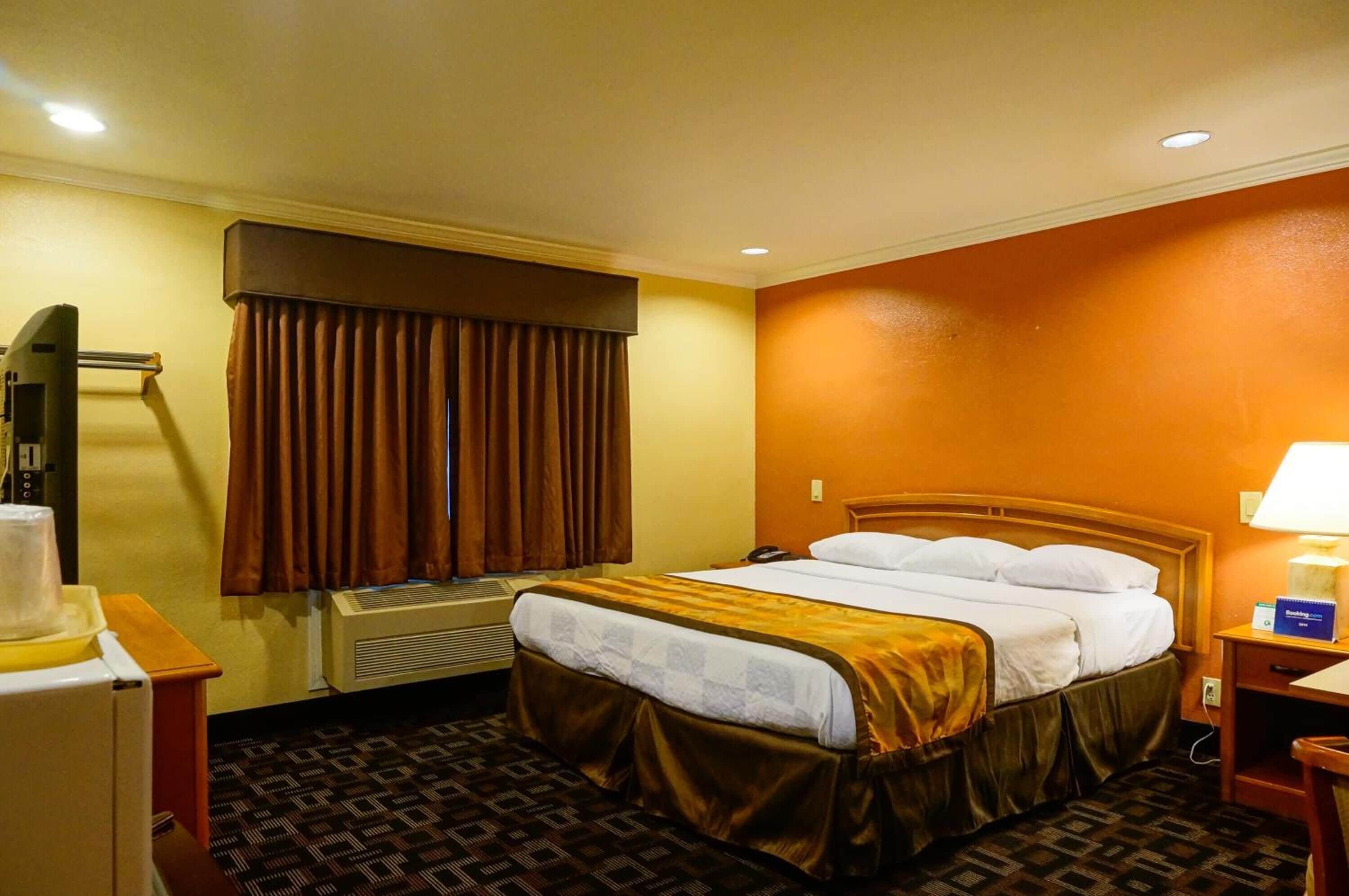 A hotel room with a bed, a desk with a lamp, a telephone, and an air conditioning unit.