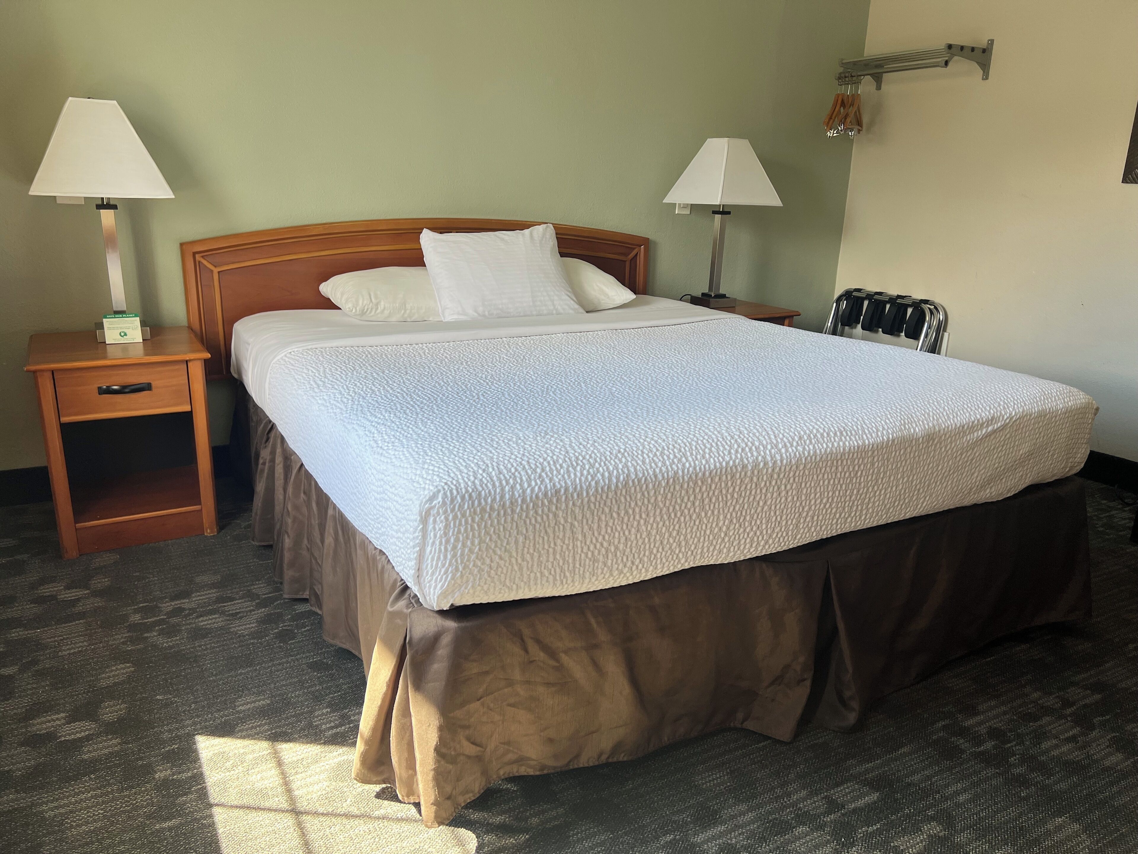 A hotel room with a large bed, two bedside tables with lamps, a wooden nightstand, and a wall-mounted radiator.