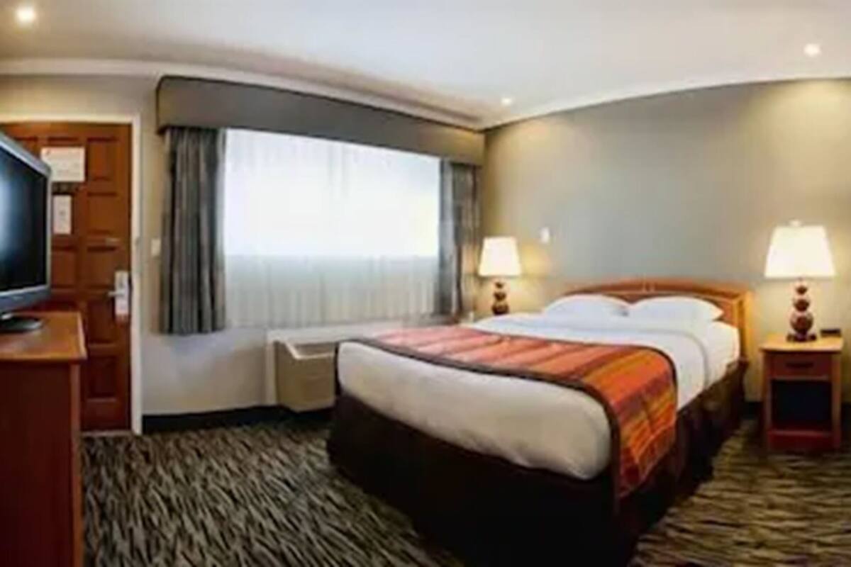 Habitación de hotel con una cama grande, dos mesitas de noche con lámparas, una televisión y vistas al exterior a través de una ventana.