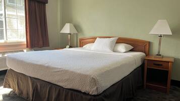 A hotel room with a large bed, two bedside tables, a window with curtains, and a wall-mounted lamp.