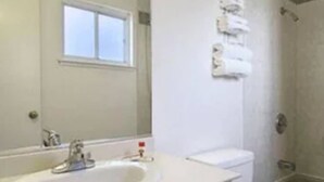 A bathroom with a white sink, a mirror, a window, and a shower area. - Hotel Parmani (Palo Alto)