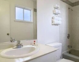Un baño con lavamanos blanco, espejo, ventana y zona de ducha.
