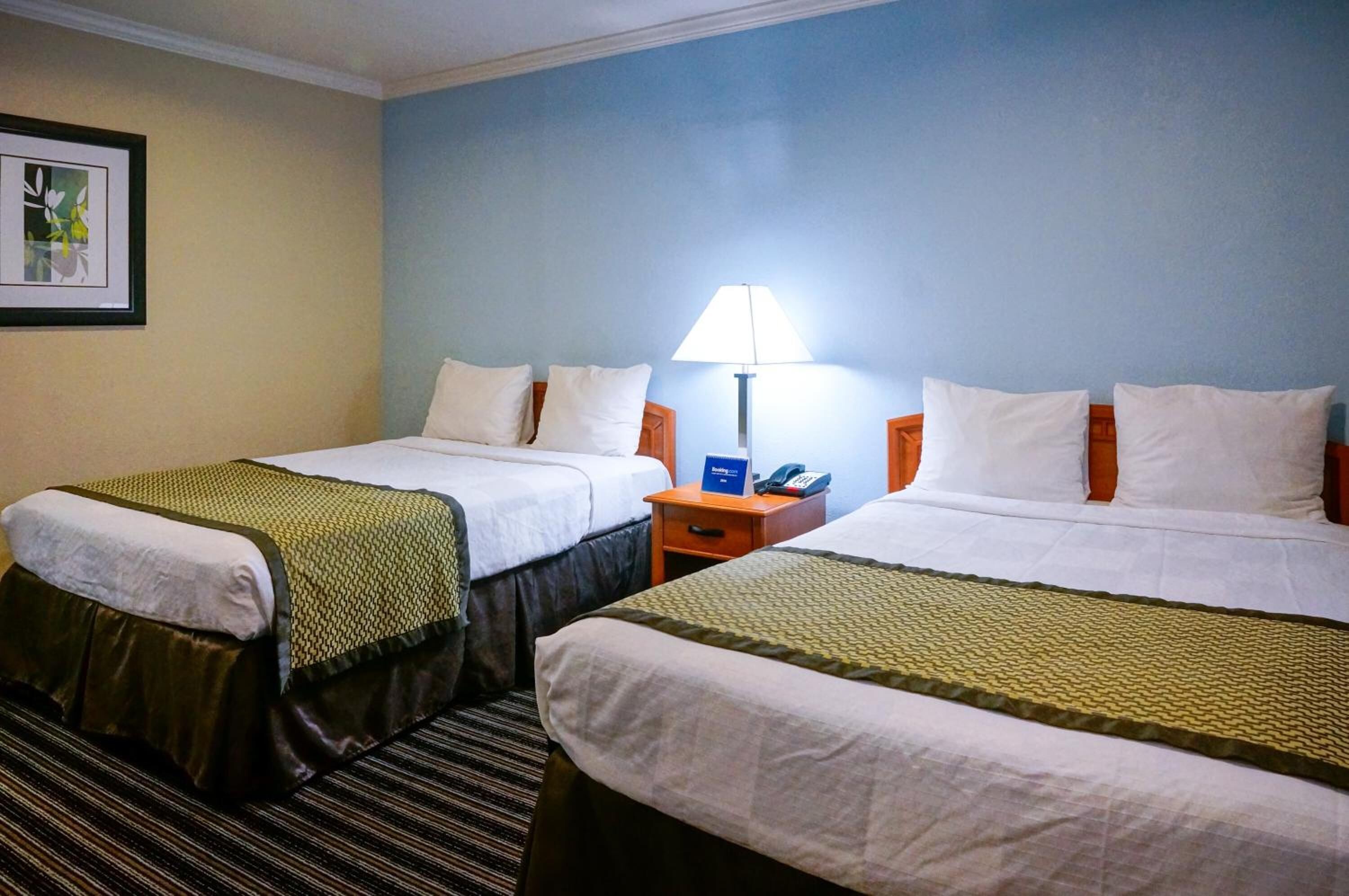 Una habitación de hotel con dos camas, una mesita de noche con lámpara y un cuadro en la pared.