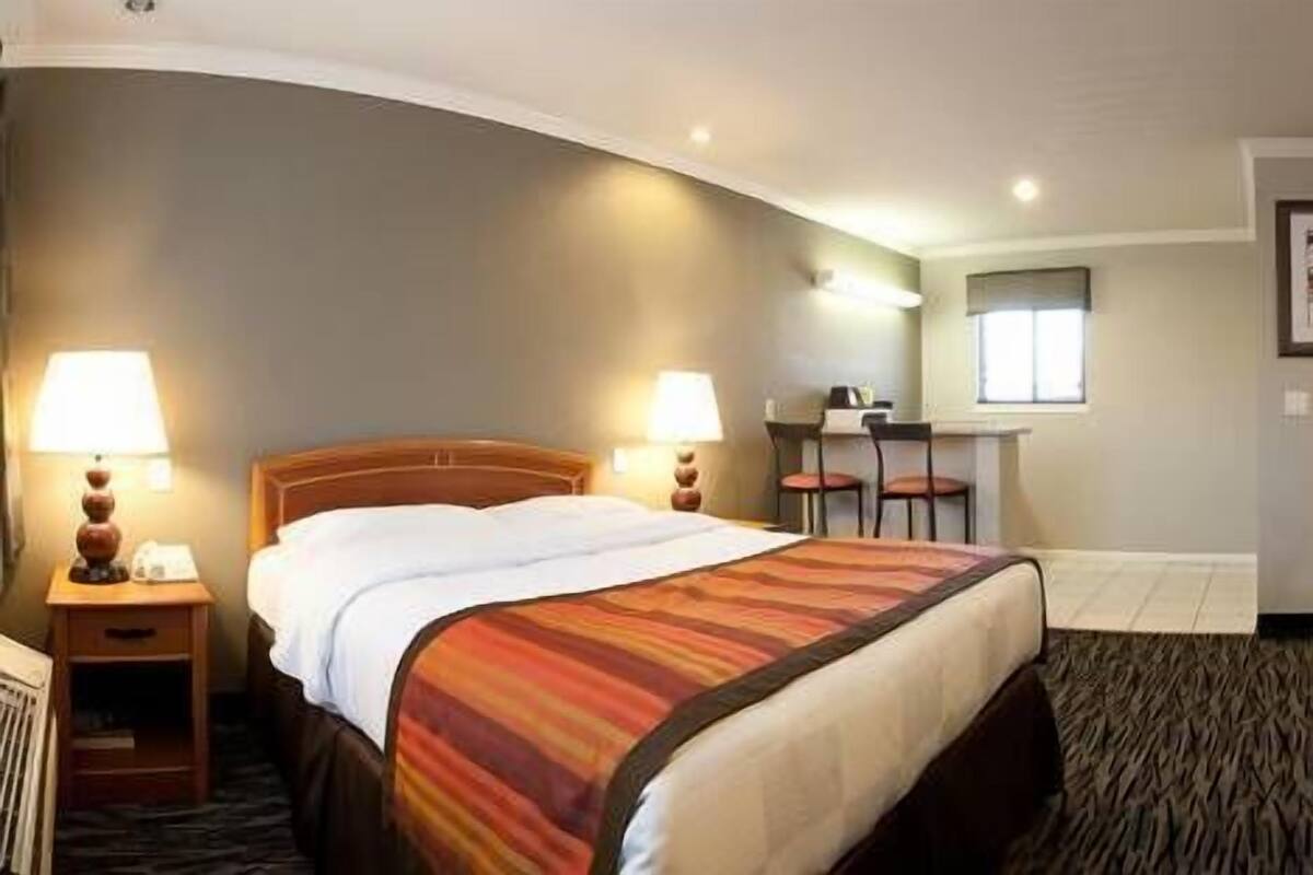 Habitación de hotel con cama, dos mesitas de noche con lámparas, un escritorio y una silla, y un ventanal pequeño.